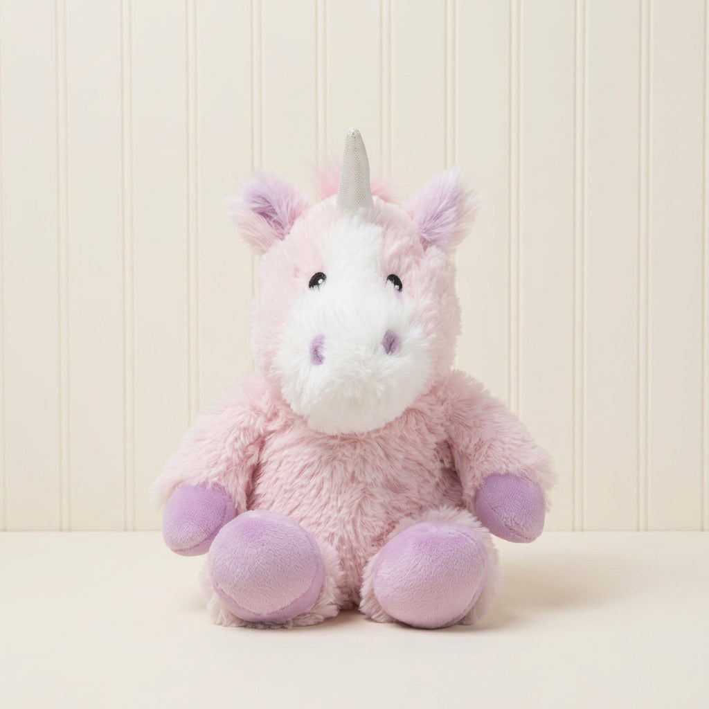 A pink and white plush unicorn toy with a white horn, sitting centered against a rustic wooden plank backdrop.