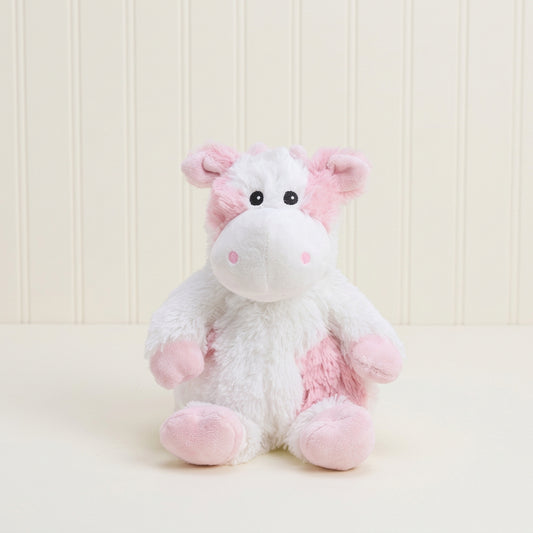 A small plush cow toy with a white body, pink ears, pink hooves, and pink patches on its face and body, sitting against a plain light beige studio background.