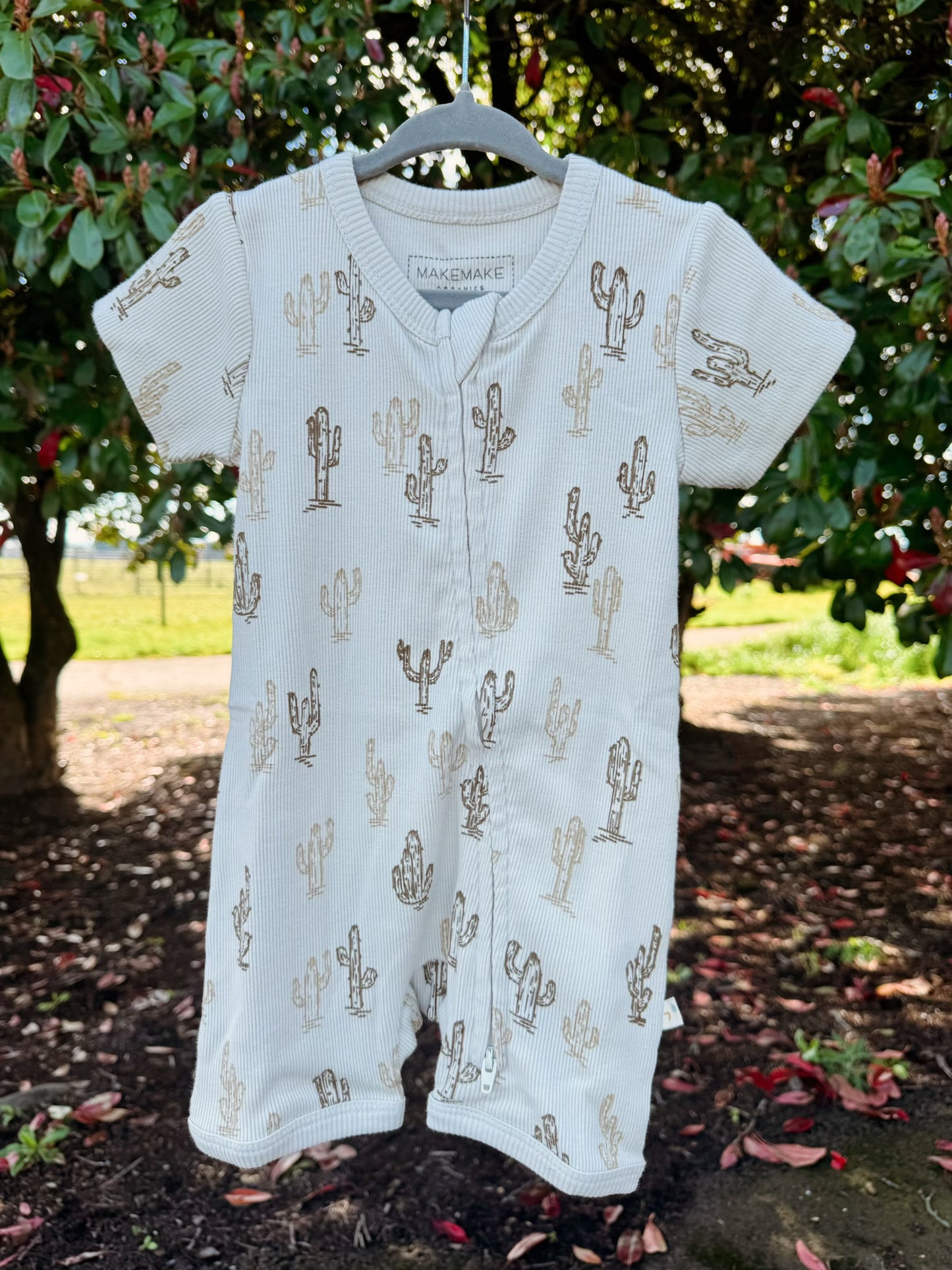 Baby romper with cactus pattern on a hanger against a natural background