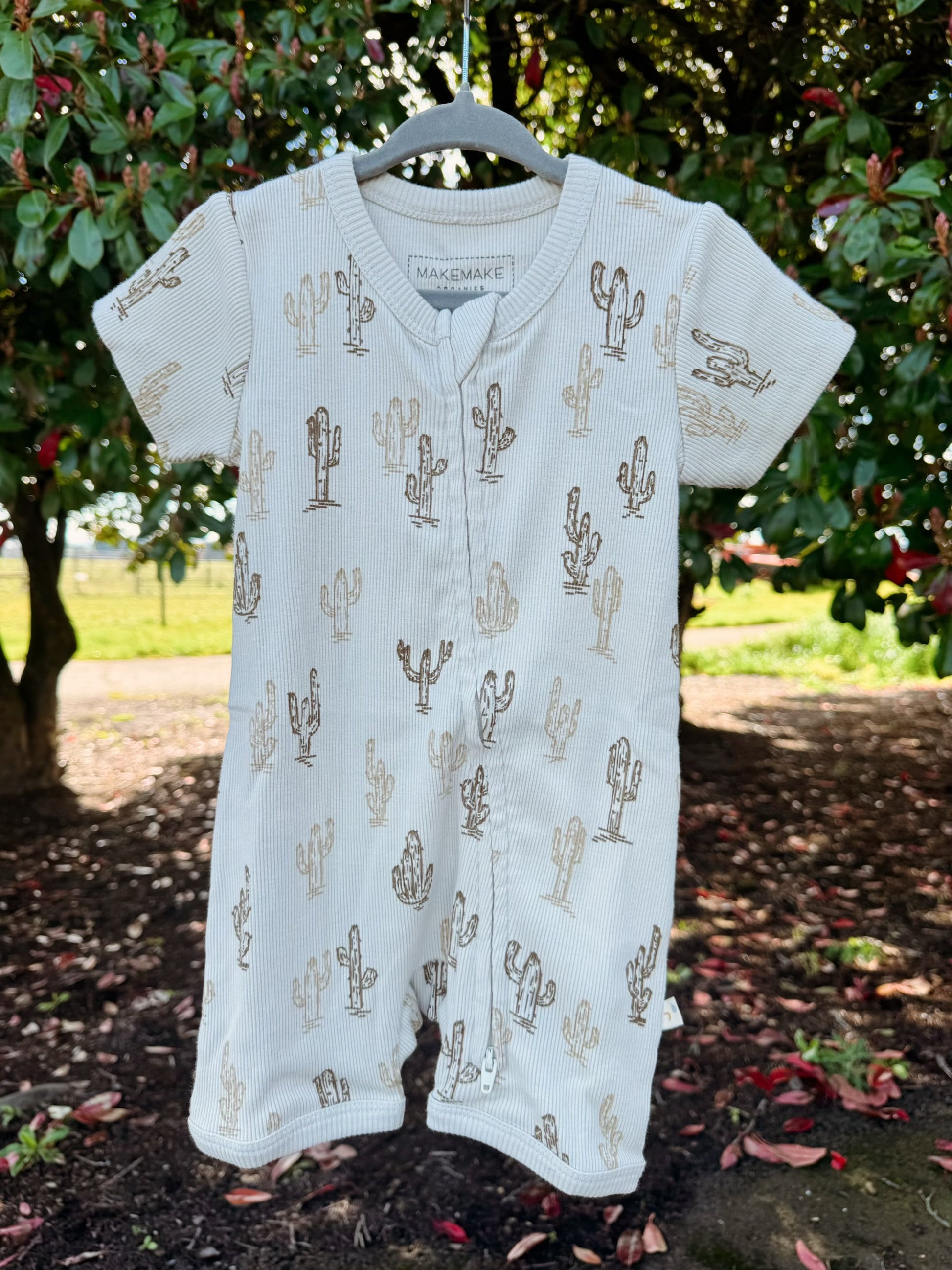 Baby romper with cactus pattern on a hanger against a natural background