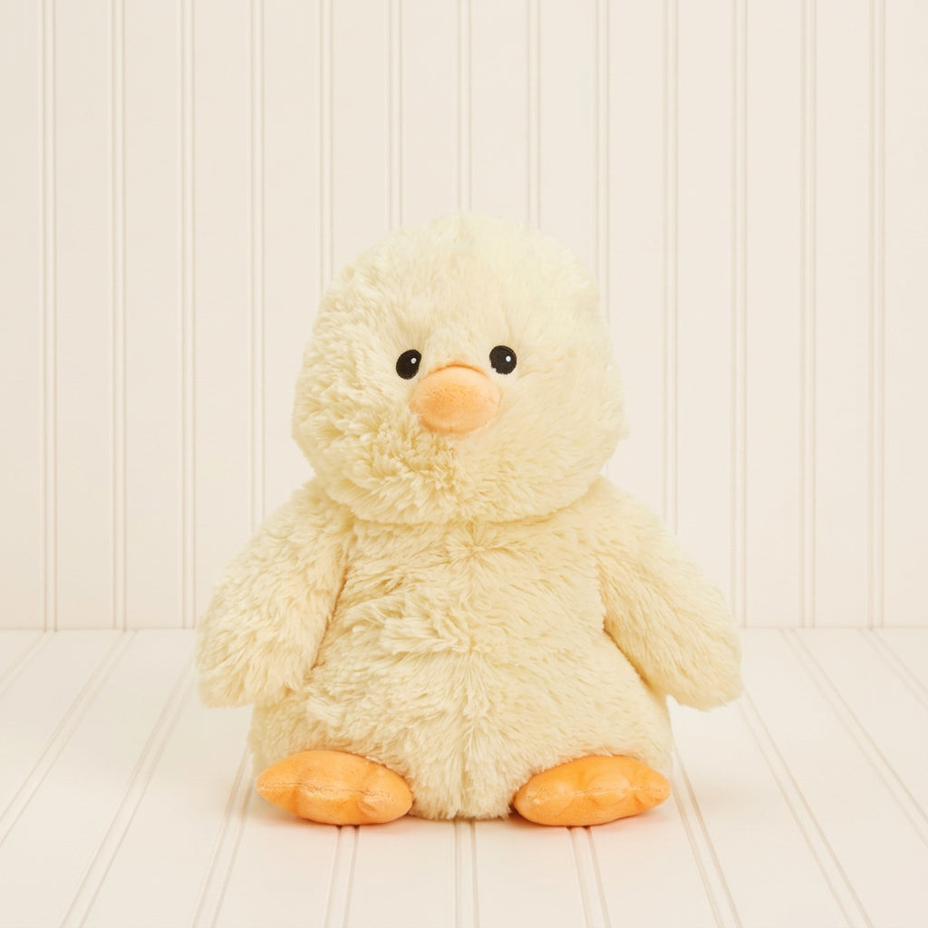 A fluffy cream-colored plush duck toy with orange feet and beak, sitting against a solid light beige background.